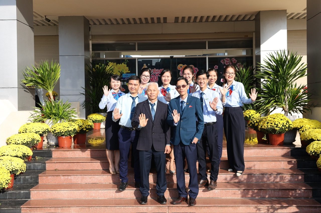 Anh Châu cùng các đồng nghiệp ngân hàng trong tấm ảnh chụp đầu xuân trước trụ sở, giữa những chậu cúc vàng.