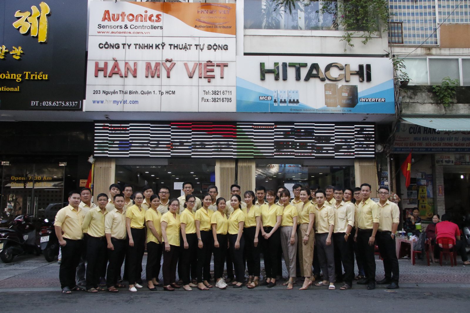 Đại gia đình Hàn Mỹ Việt trong đồng phục vàng trước trụ sở công ty, nơi anh Hùng gắn bó từ năm 1997 khi công ty còn là một văn phòng nhỏ.