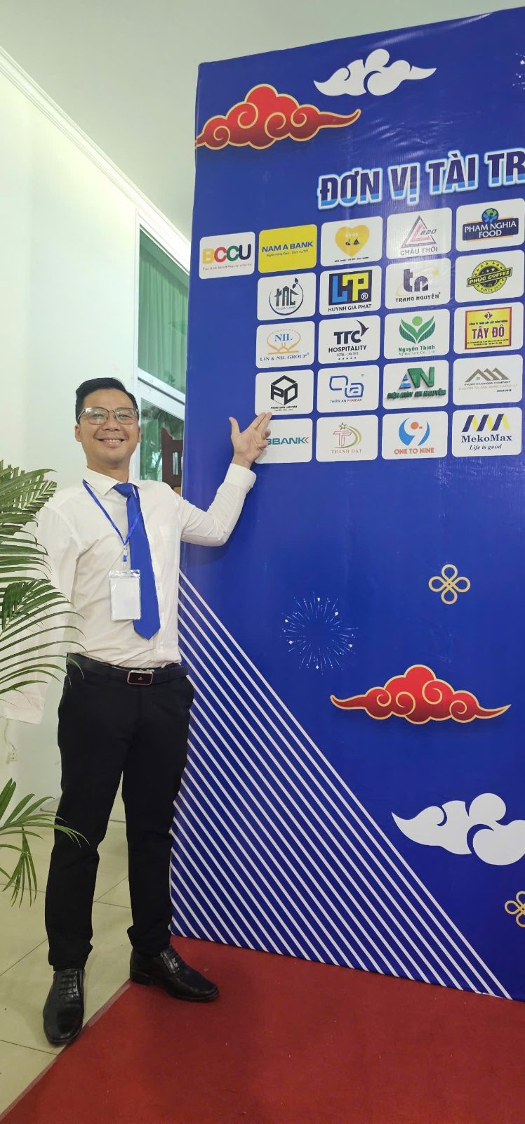 Anh Phong bên bảng đơn vị tài trợ của một chương trình, tay chỉ vào logo Phong Dinh Law Firm, công ty luật anh gây dựng từ con số không.