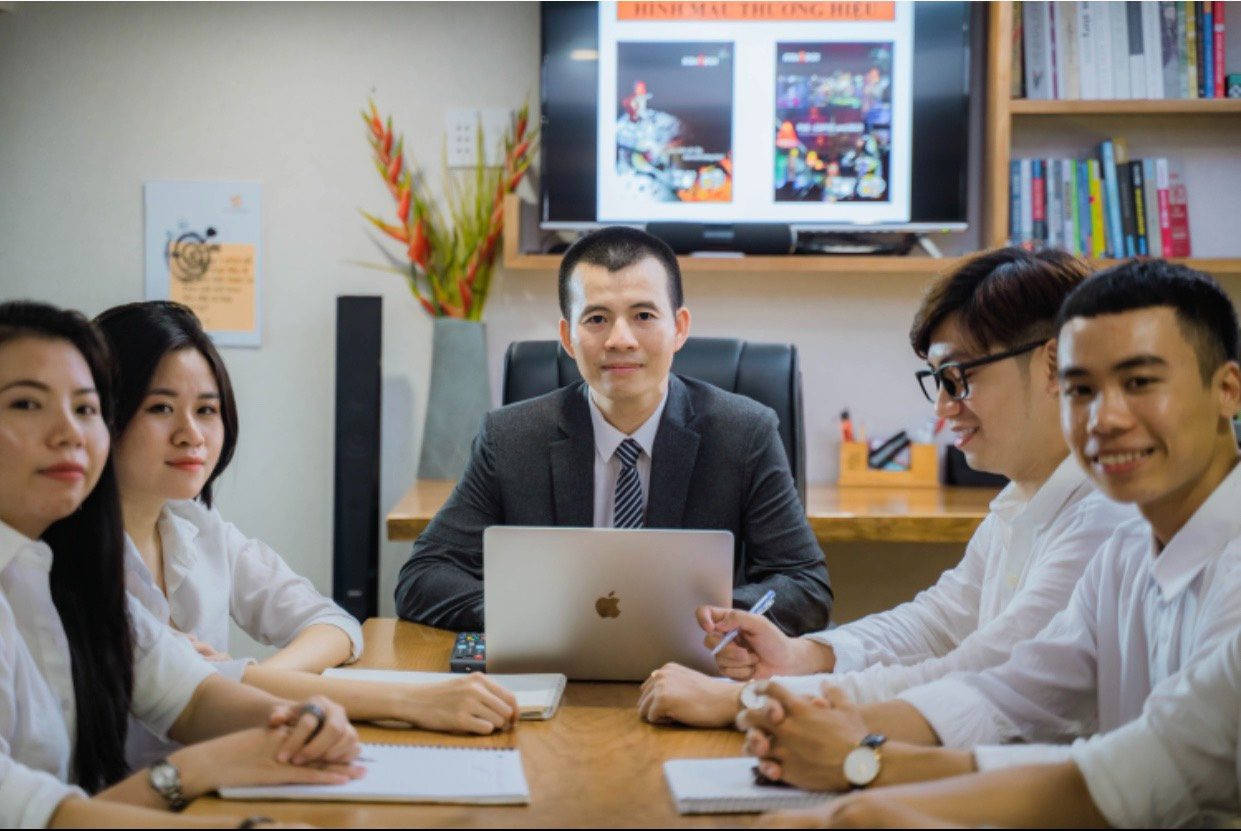 Anh Nguyễn Tiến Năm (giữa) ngồi họp cùng đội ngũ trẻ của mình, màn hình phía sau đang chiếu phần hình mẫu thương hiệu.