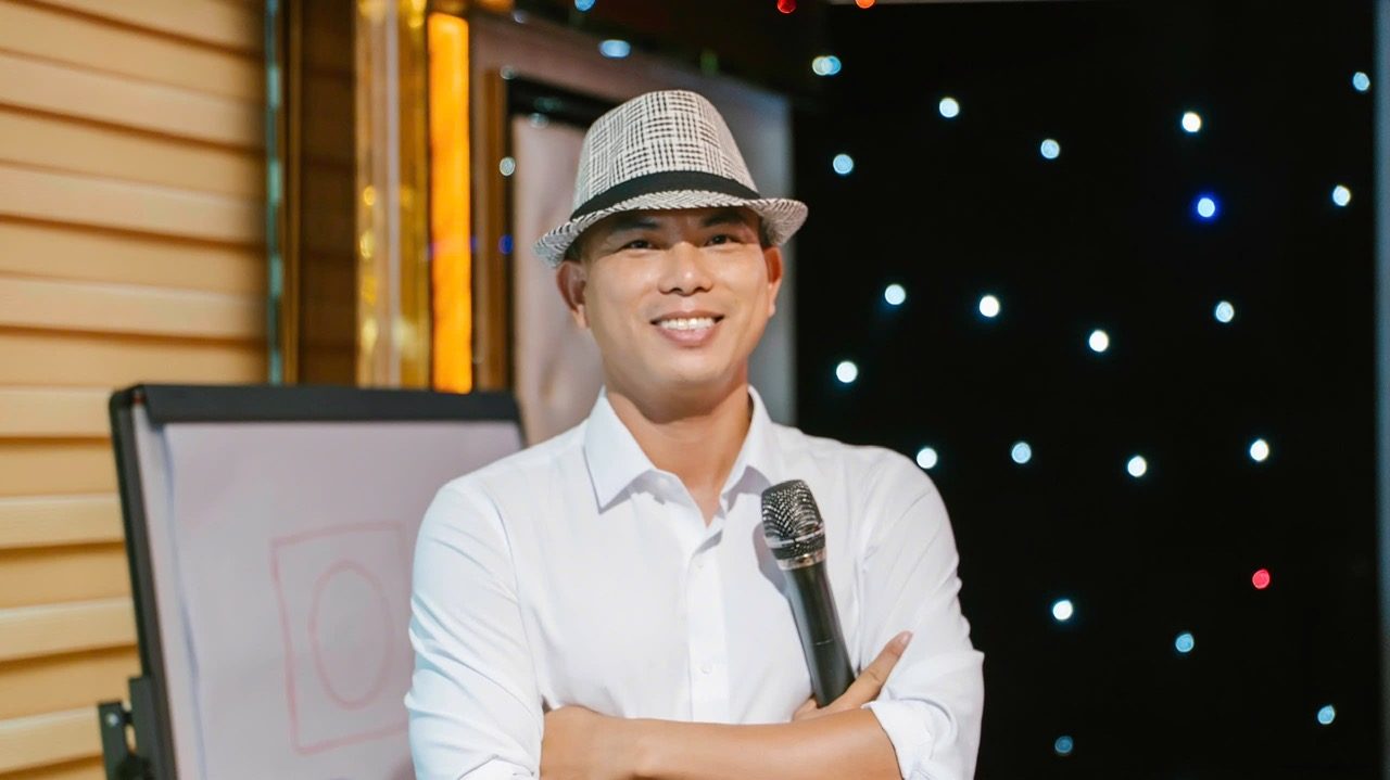 Anh Vũ Văn Lễ, người mang biệt danh Vua Truyền Lửa, cầm micro bên tấm bảng lật trong một buổi đào tạo